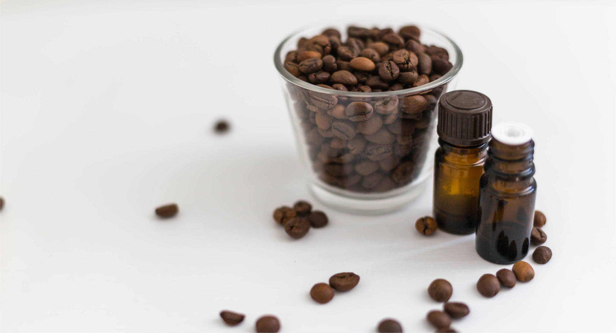 Coffee beans beside two small amber bottles on a pale surface.
