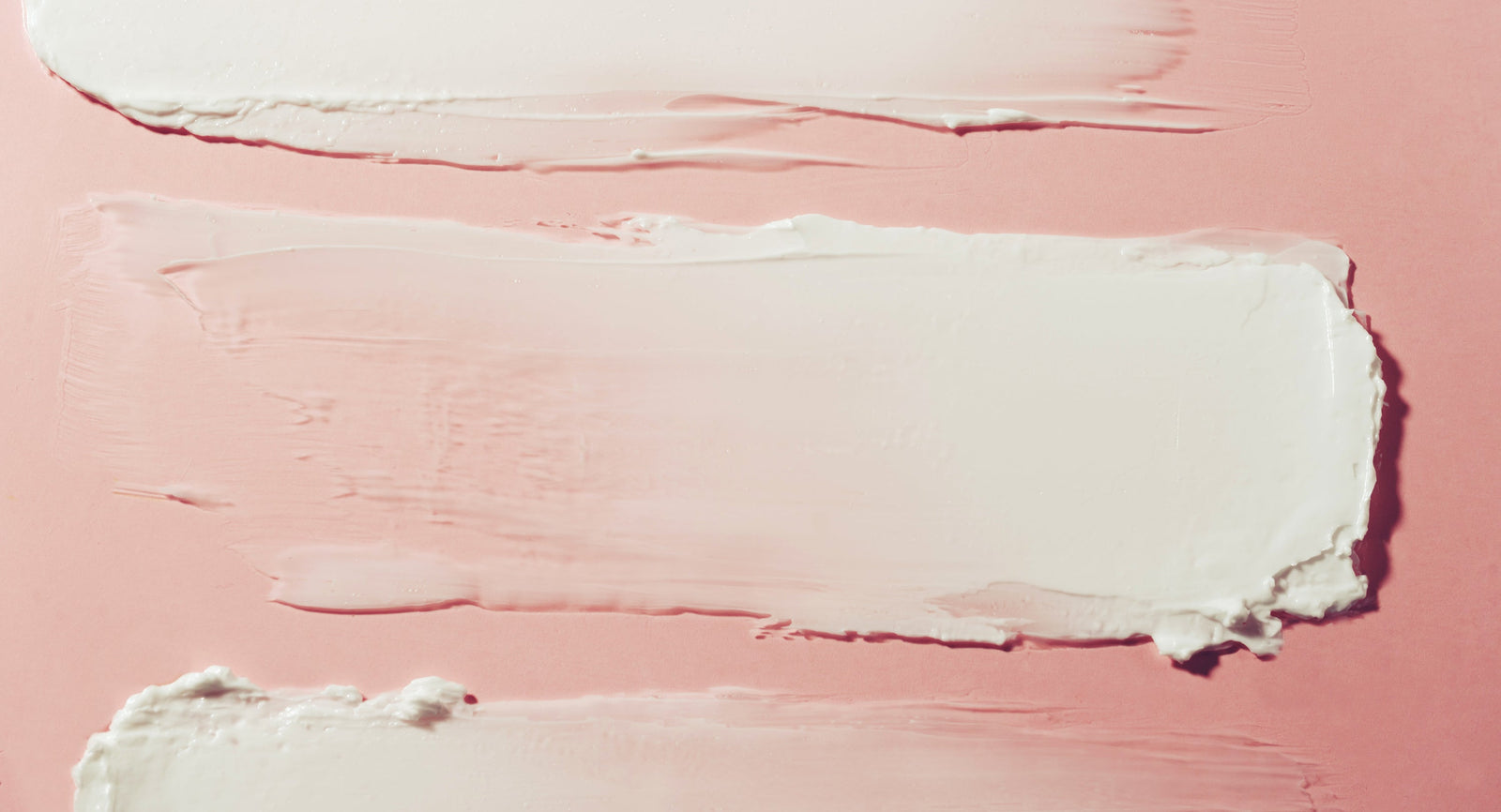 Cream-colored cosmetic swatches on a pink surface