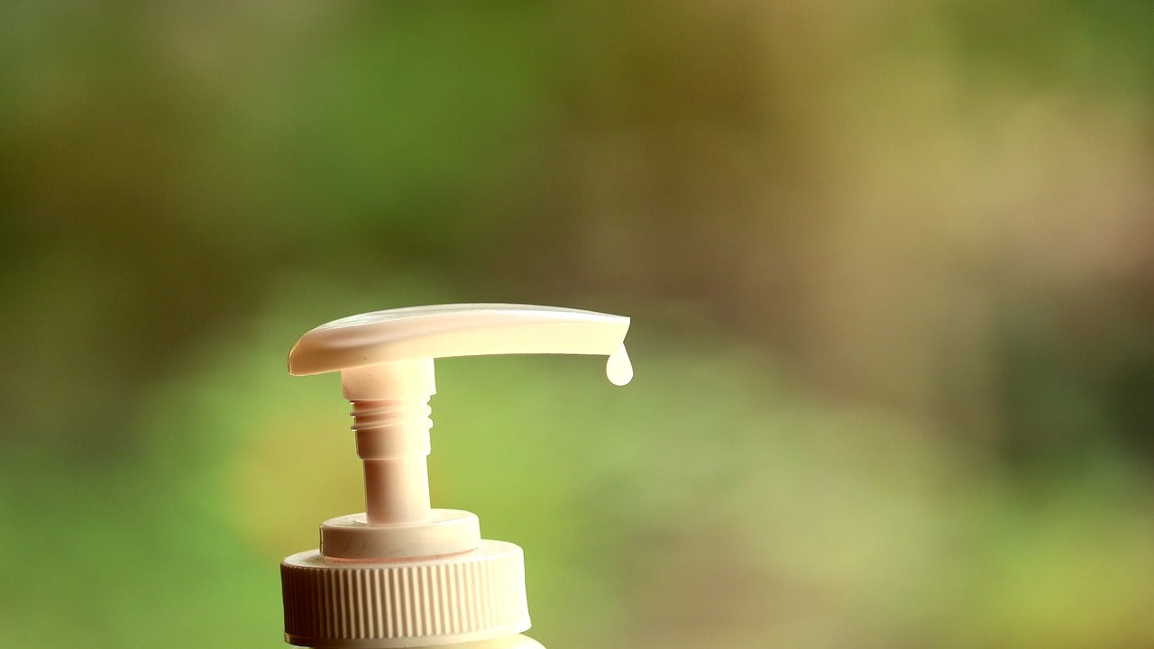 Drop of skincare product at the tip of a white pump dispenser against a green background.