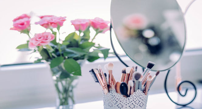 Clean makeup brushes beside a mirror and pink flowers