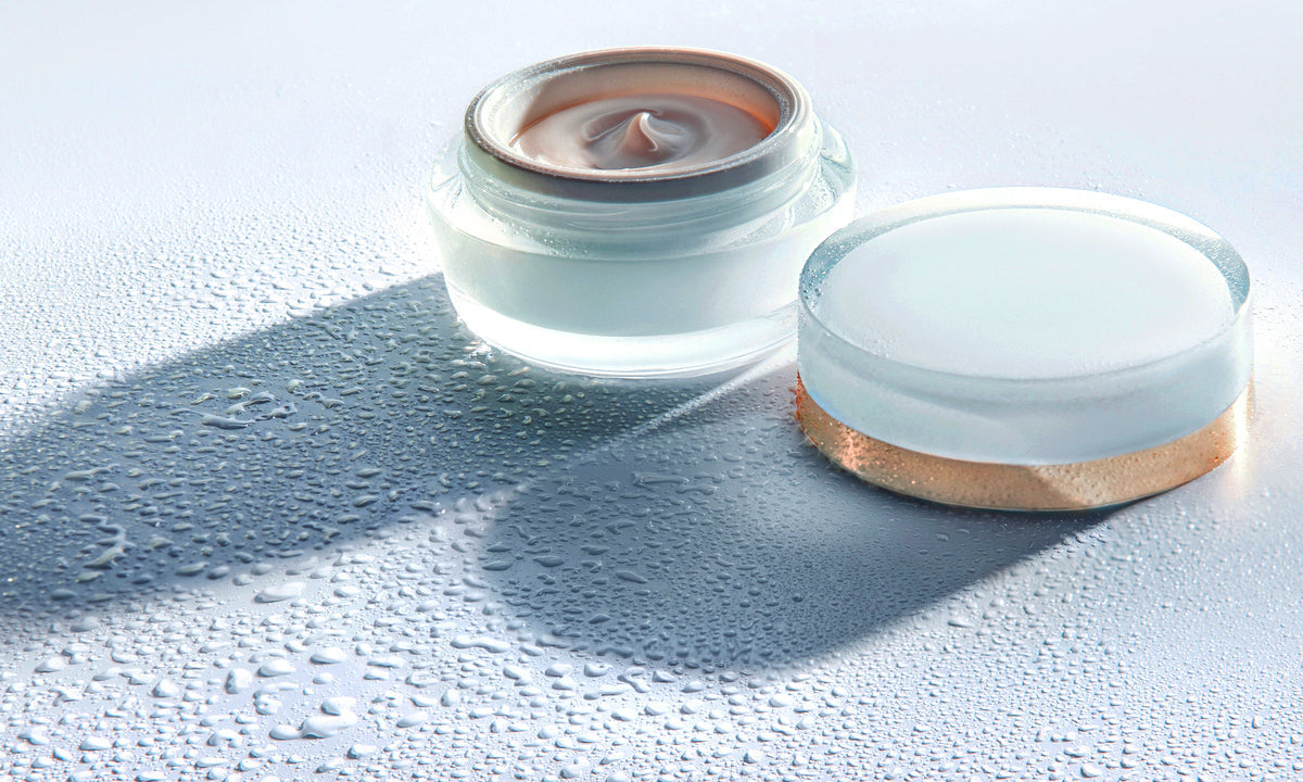 Two cosmetic cream jars on a pale blue surface