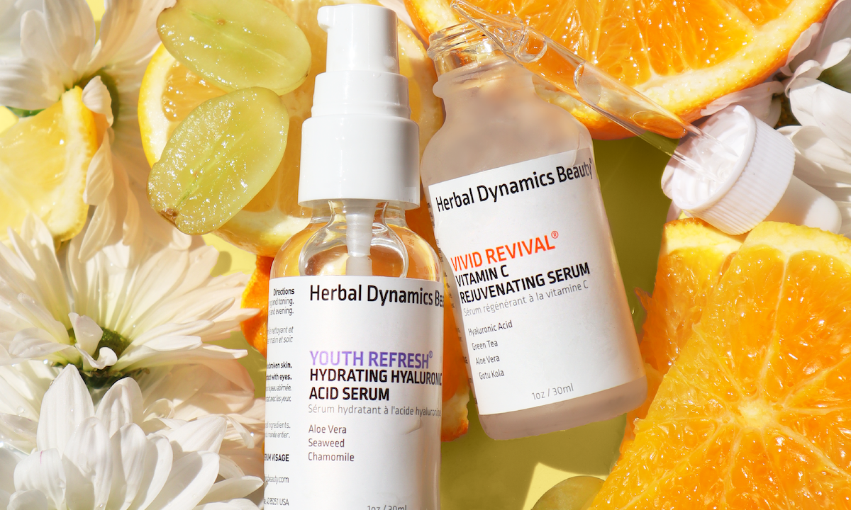 Herbal Dynamics Beauty Youth Refresh and Vivid Revival serum bottles beside citrus, grapes and flowers.